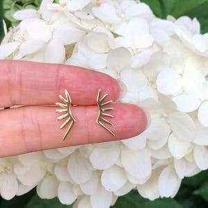 May include: A pair of gold earrings with a sunburst design. The earrings are small and delicate, and they would make a great gift for a friend or loved one.