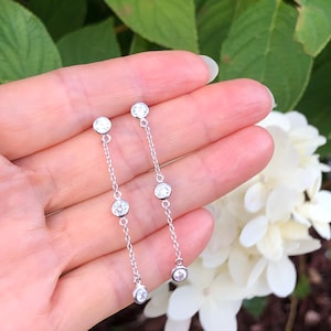 May include: A pair of silver dangle earrings with small round clear stones. The earrings have a delicate chain design with four stones on each earring.