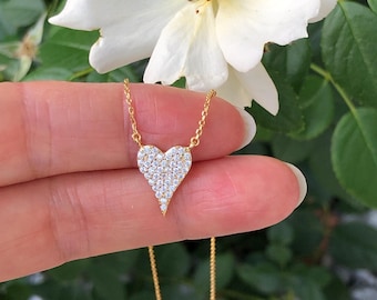 May include: A gold chain necklace with a small, heart-shaped pendant encrusted with clear cubic zirconia stones. The pendant is on a delicate chain.