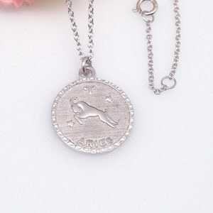 May include: Silver necklace with a round pendant featuring the zodiac sign Aries. The pendant has a detailed design of the ram and the word "Aries" inscribed below.