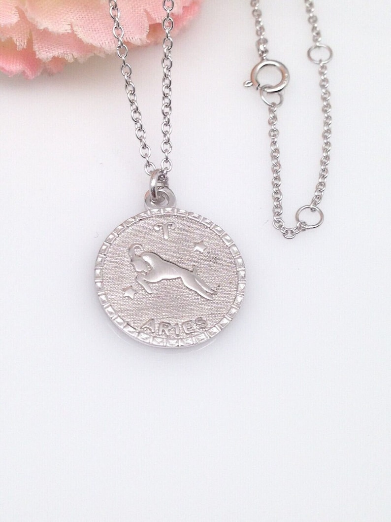 May include: Silver necklace with a round pendant featuring the zodiac sign Aries. The pendant has a detailed design of the ram and the word "Aries" inscribed below.
