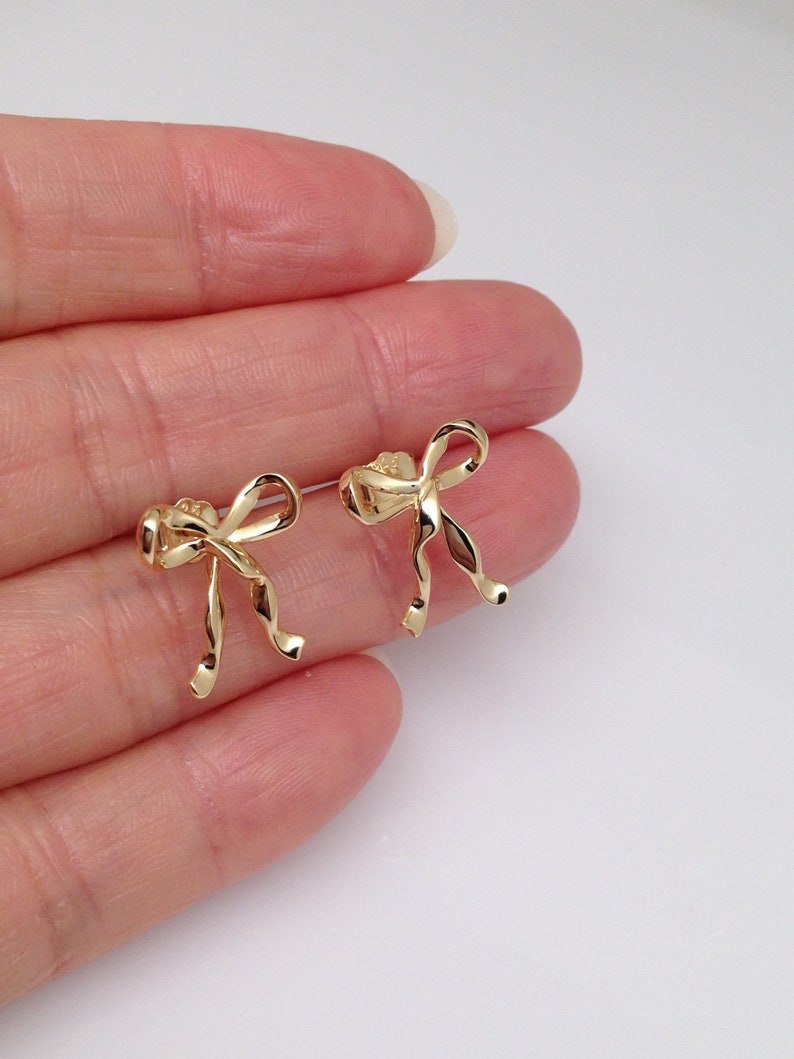 Puede incluir: Un par de pendientes de lazo de color dorado. Los lazos est&aacute;n retorcidos y tienen un aspecto delicado y femenino.