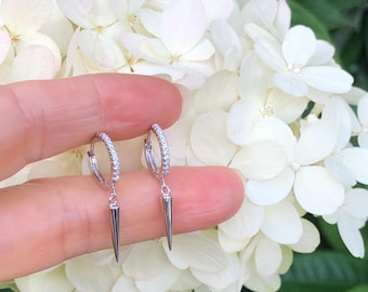 May include: A pair of silver hoop earrings with a row of small clear stones around the hoop and a pointed silver dangle.