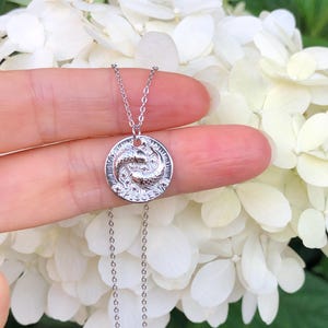 May include: A silver necklace with a round pendant featuring a detailed design of two intertwined snakes. The necklace is on a silver chain.