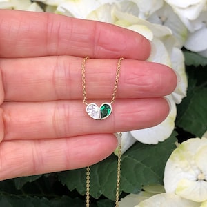 May include: A delicate gold chain necklace with a pendant featuring two teardrop-shaped gemstones. One gemstone is clear and the other is a vibrant green.