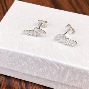 May include: A pair of silver earrings with a leaf design and clear cubic zirconia stones.