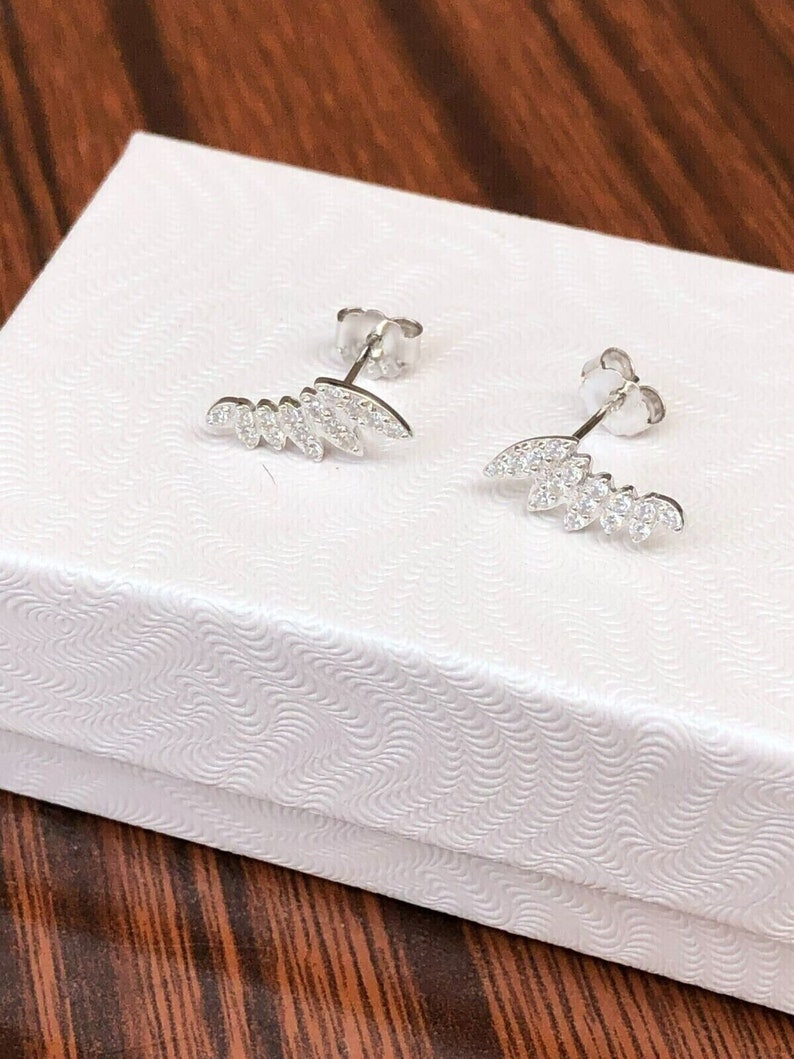 May include: A pair of silver earrings with a leaf design and clear cubic zirconia stones.