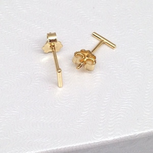 K&ouml;nnte beinhalten: Ein Paar goldfarbene Ohrstecker mit einem geraden Stabdesign. Die Ohrringe haben einen Stift und einen Schmetterlingsverschluss.