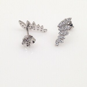 May include: A pair of silver earrings with a leaf design. The earrings are adorned with small, clear stones.