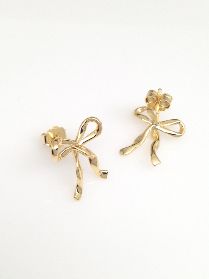 Puede incluir: Un par de pendientes de color dorado en forma de lazo. Los pendientes est&aacute;n hechos de metal retorcido y tienen un dise&ntilde;o simple y elegante.