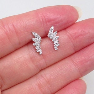 May include: A pair of silver earrings with a delicate, curved design. Each earring features a row of small, clear cubic zirconia stones.