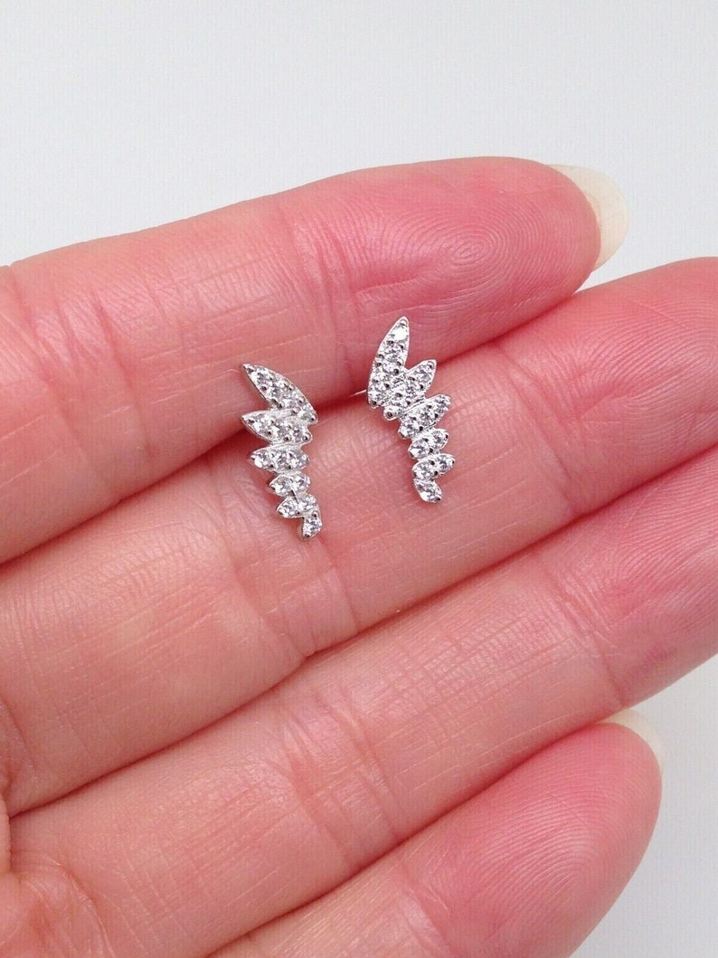 May include: A pair of silver earrings with a delicate, curved design. Each earring features a row of small, clear cubic zirconia stones.