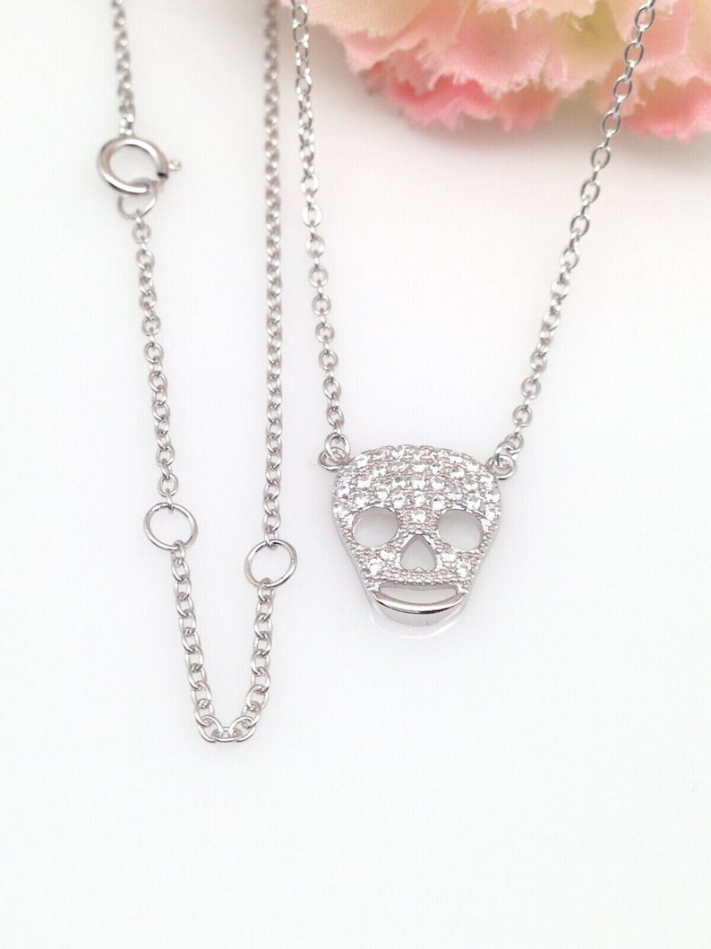 Puede incluir: Un collar de cadena de plata con un peque&ntilde;o colgante de calavera pav&eacute;. El colgante est&aacute; hecho de plata y est&aacute; cubierto de peque&ntilde;as piedras de circonita c&uacute;bica transparentes.