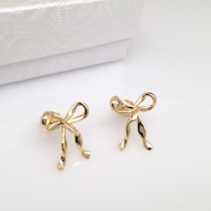 Puede incluir: Un par de pendientes de color dorado en forma de lazo. Los pendientes est&aacute;n hechos de un dise&ntilde;o de metal retorcido.