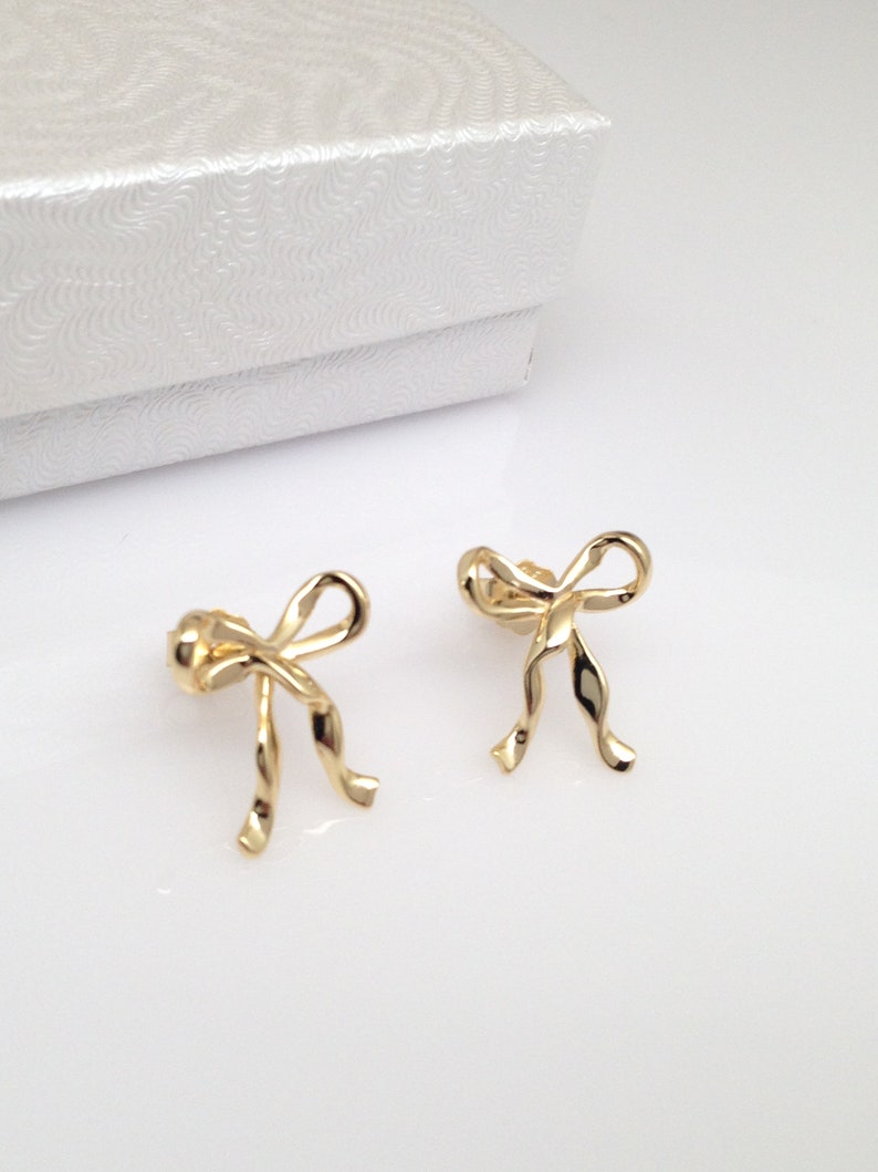 Puede incluir: Un par de pendientes de color dorado en forma de lazo. Los pendientes est&aacute;n hechos de un dise&ntilde;o de metal retorcido.