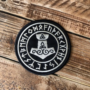 May include: A black and white embroidered patch with a stylized hammer and runes. The runes spell "Mjolnir" in Old Norse.