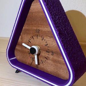 Klein klokje, driehoekig van vorm, met mahoniehouten wijzerplaat, gekleurde rand en modern design.