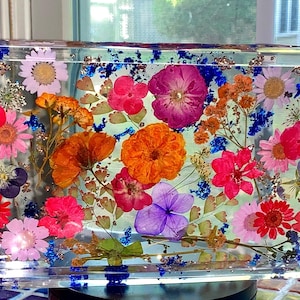 May include: A clear resin tray filled with a vibrant assortment of dried flowers in shades of pink, red, orange, and purple. The tray's edges are decorated with blue accents, creating a colorful and decorative piece.