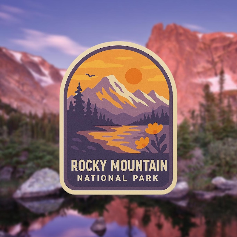 May include: A sticker featuring a scenic illustration of the Rocky Mountain National Park. The design includes a mountain range, a river, and a sunset. The text "Rocky Mountain National Park" is displayed at the bottom of the sticker.
