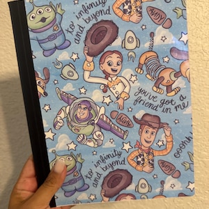 May include: A notebook with a blue cover featuring illustrations of characters from the Toy Story movie franchise. The cover includes the phrases "to infinity and beyond" and "you've got a friend in me."