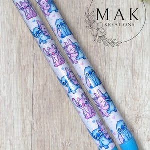 May include: Two pens with a white background, featuring cartoon characters in blue and pink. The pens have blue tips and black tops. The text "MAK KREATIONS" is in a circle in the background.