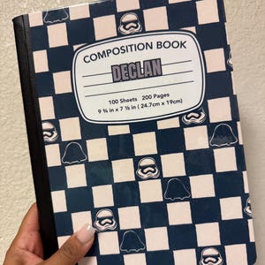 May include: Composition book with a navy blue and white checkered pattern, featuring Stormtrooper helmet and ghost graphics. The cover includes the name "DECLAN" and the text "COMPOSITION BOOK". The notebook measures 9 3/4 in x 7 1/2 in.