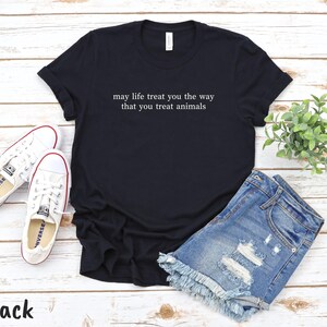 May include: Black t-shirt with white text: "may life treat you the way that you treat animals". The image includes denim shorts, white trainers, and a small green plant. The word "Black" is at the bottom.