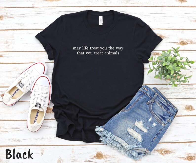 May include: Black t-shirt with white text: "may life treat you the way that you treat animals". The image includes denim shorts, white trainers, and a small green plant. The word "Black" is at the bottom.
