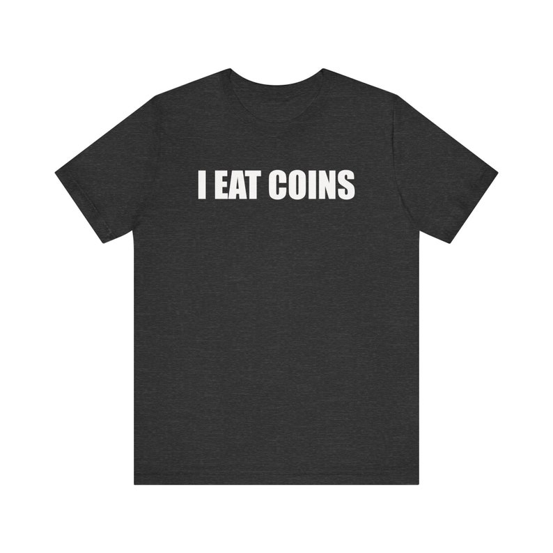 May include: Dark gray t-shirt with the white text "I EAT COINS" across the chest. The shirt is a short-sleeved crew neck style, made of a soft material. The text is in a bold, sans-serif font.