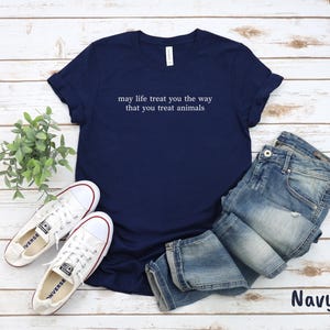 May include: Navy blue t-shirt with white text: "may life treat you the way that you treat animals". The image includes blue jeans and white trainers. The word "Navy" is visible in the bottom right corner.