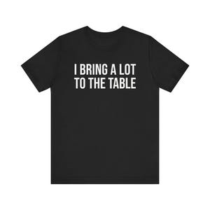 Może przedstawiać: Czarny T-shirt z białym napisem "Wnoszę wiele do stołu."