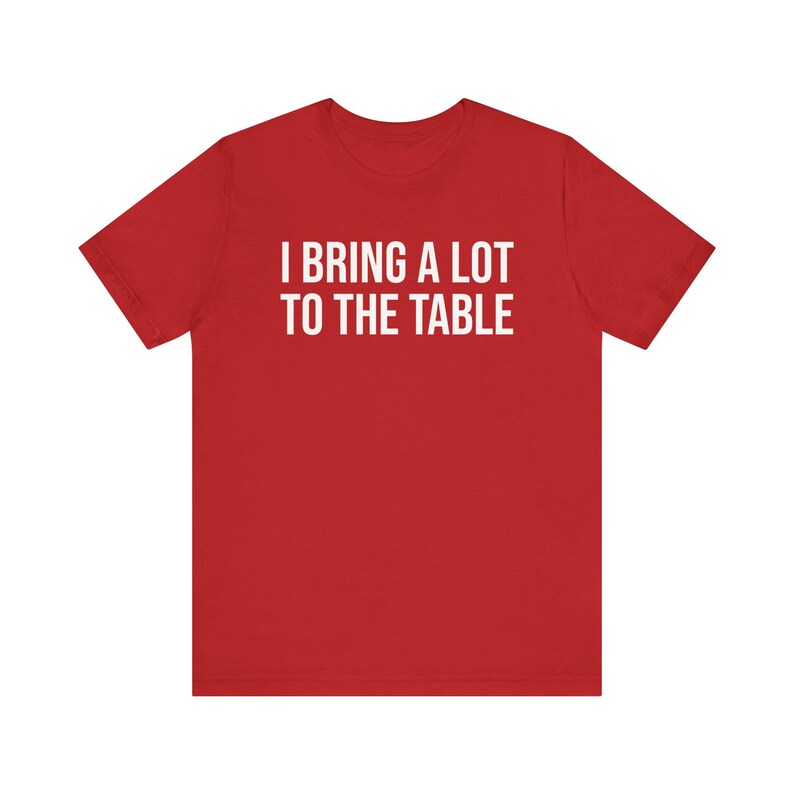 Może przedstawiać: Czerwony T-shirt z kr&oacute;tkim rękawem z białym napisem "Wnoszę wiele do stołu."