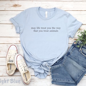 May include: Pale blue t-shirt featuring the quote "may life treat you the way that you treat animals." The image includes denim shorts and white trainers.