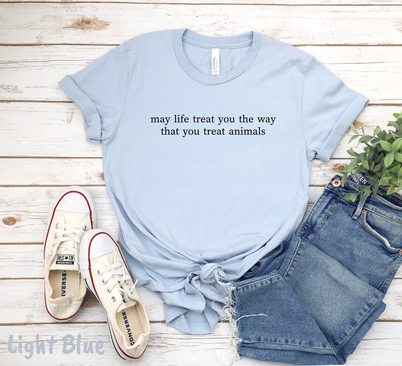 May include: Pale blue t-shirt featuring the quote "may life treat you the way that you treat animals." The image includes denim shorts and white trainers.