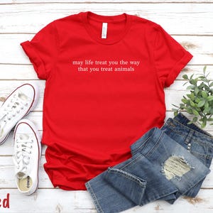 May include: A bright red t-shirt with the white text "may life treat you the way that you treat animals". The image also shows blue denim jeans and white trainers. The word "Red" is in the bottom left corner.