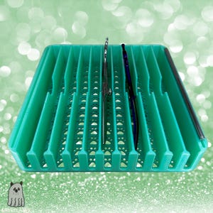 Könnte beinhalten: Ein teal-farbener Organizer mit vertikalen Schlitzen, der eine silberne Schere und einen blauen Stift hält. Der Organizer hat ein Pfotenabdruck-Design auf der Unterseite und eine schwarze Umrandung.