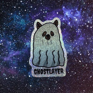 Könnte beinhalten: Ein holografischer Aufkleber mit einem geisterhaften Charakter mit bärenartigen Ohren und einer runden Nase. Auf dem Aufkleber steht das Wort "GHOSTLAYER" am unteren Rand. Der Hintergrund ist eine Galaxie aus Blau-, Lila- und Weißtönen.