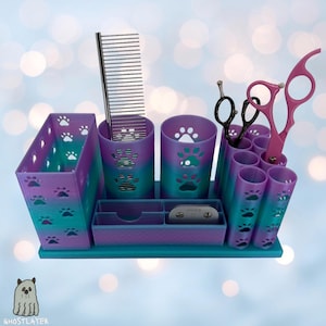 May include: A multi-compartment pet grooming organizer in shades of purple and teal, featuring paw print cutouts. It holds grooming tools like scissors, combs, and clippers. The organizer is designed to keep pet grooming supplies neat and accessible.