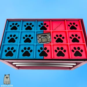 May include: A pink and black pet grooming tool organizer with blue and red compartments. Each compartment features a black paw print design. A silver grooming blade is in the center. The text "GHOSTLAYER" is visible.