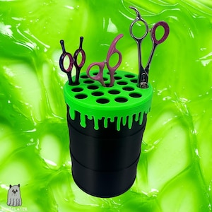 May include: A black and green cylindrical organizer with multiple pairs of scissors. The top of the organizer is bright green with several holes for the scissors. The scissors have various colors, including pink and silver.