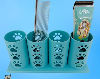 Op de afbeelding: Een turquoise organizer met vier bekers en uitgesneden pootafdrukken, met daarin een zilveren metalen kam en een professionele Kenchii-tondeuse voor huisdieren met een afbeelding van een langharige hond op de voorzijde.