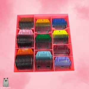 May include: A pink organizer box filled with nine different colored hair clipper guards. The guards are in shades of brown, yellow, blue, pink, green, orange, teal, burgundy, and purple. The image has a pink background and a small cartoon ghost logo.