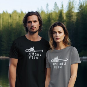 Op de afbeelding: Twee mensen dragen T-shirts met een kettingzaag afbeelding en de tekst "I just cut a big one". De persoon links draagt een zwart T-shirt en de persoon rechts draagt een grijs T-shirt.