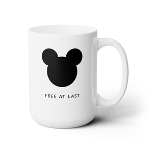 May include: White ceramic mug with a black silhouette of Mickey Mouse's head and the text "FREE AT LAST" printed on the front.