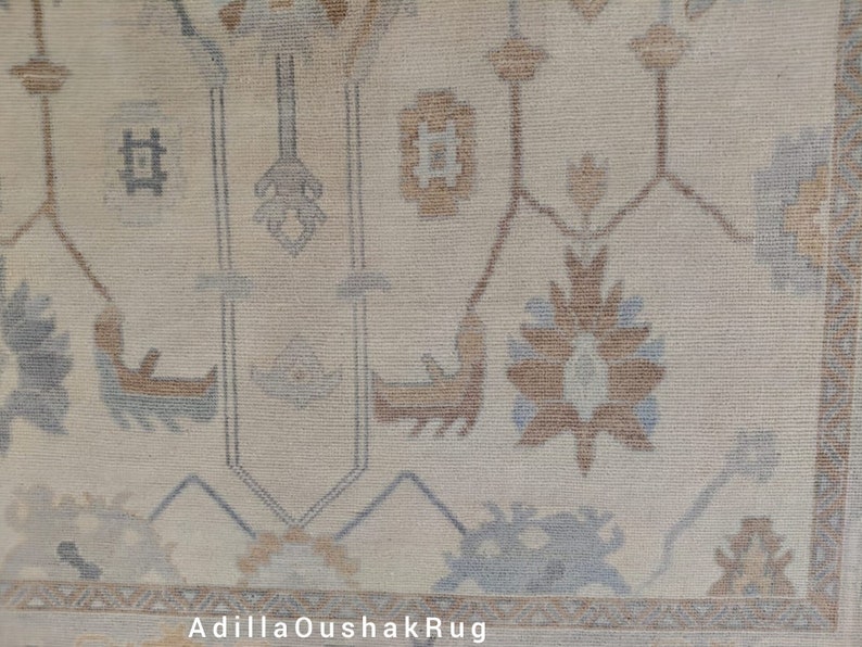 Op de afbeelding: Een beige Oushak-kleed met een traditioneel bloemenpatroon in tinten bruin en blauw. Het kleed heeft een franje rand.