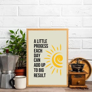 May include: A beige framed print with a yellow sun graphic and the text "A little progress each day can add up to big result".