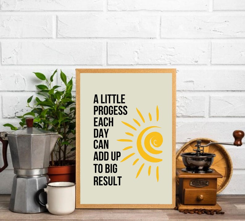 May include: A beige framed print with a yellow sun graphic and the text "A little progress each day can add up to big result".