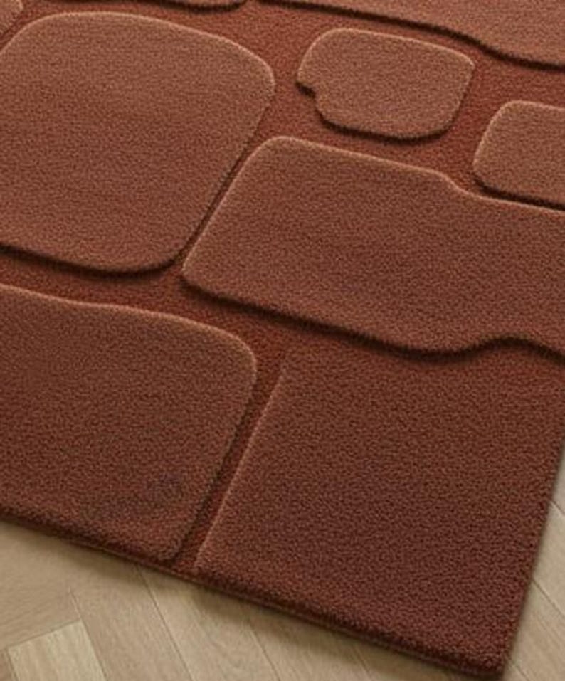 May include: A textured, rust-colored rug with a unique design. The rug features several raised, irregularly shaped sections, creating a three-dimensional effect. The overall aesthetic is modern and minimalist, suitable for various interior styles.