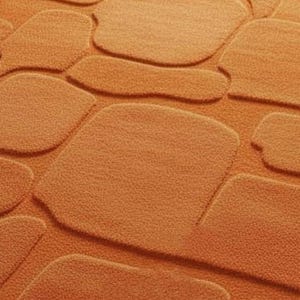 May include: Close-up of an orange bath mat with a stone-like pattern. The mat features raised, rounded shapes resembling cobblestones, creating a textured surface. The color is a warm, earthy orange.