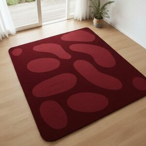 May include: A rectangular burgundy rug with a pattern of large, lighter burgundy organic shapes. The rug is placed on a light-colored wooden floor, with a window and a potted plant in the background.